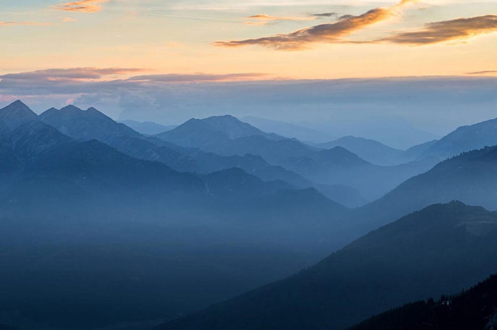 Papier peint panoramique de montagnes isolées au coucher du soleil, ciel brumeux et bleu