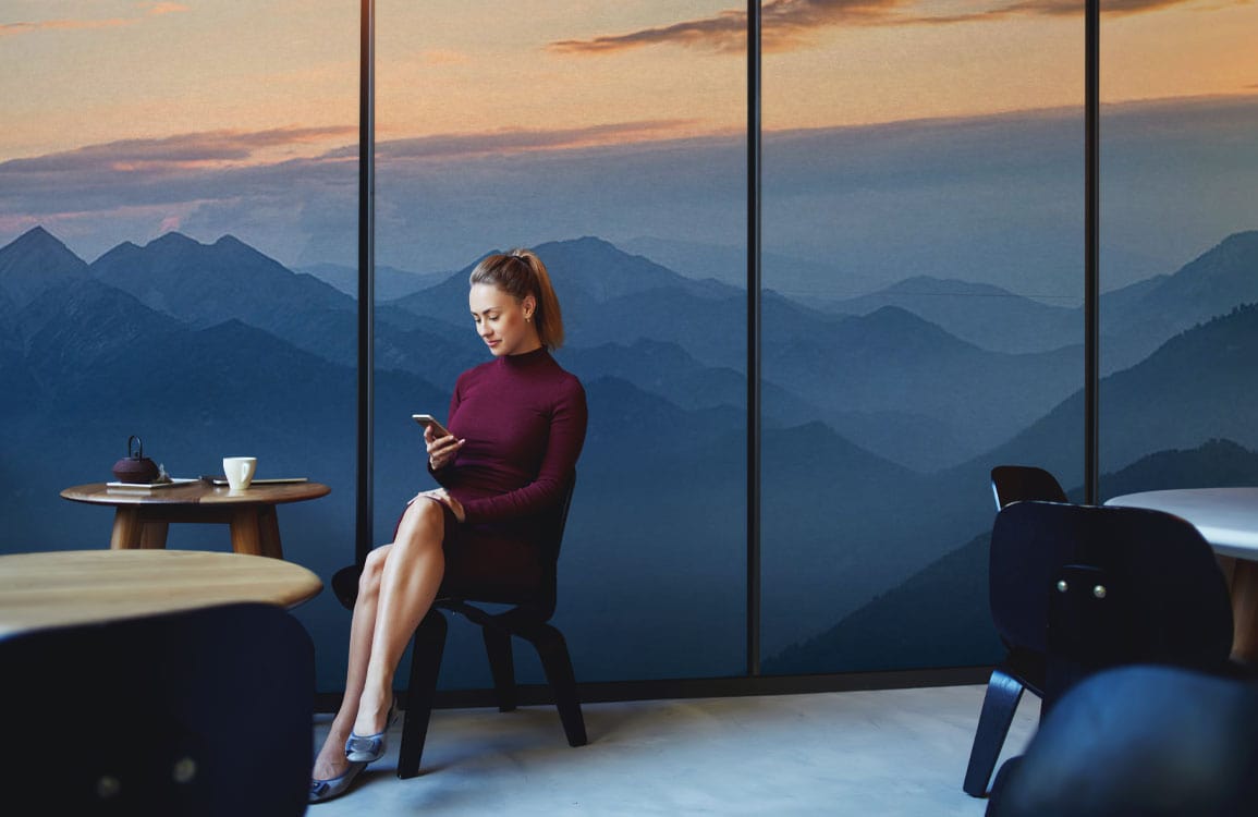 Femme en robe bordeaux tenant un smartphone devant un papier peint montagnes isolées panoramique