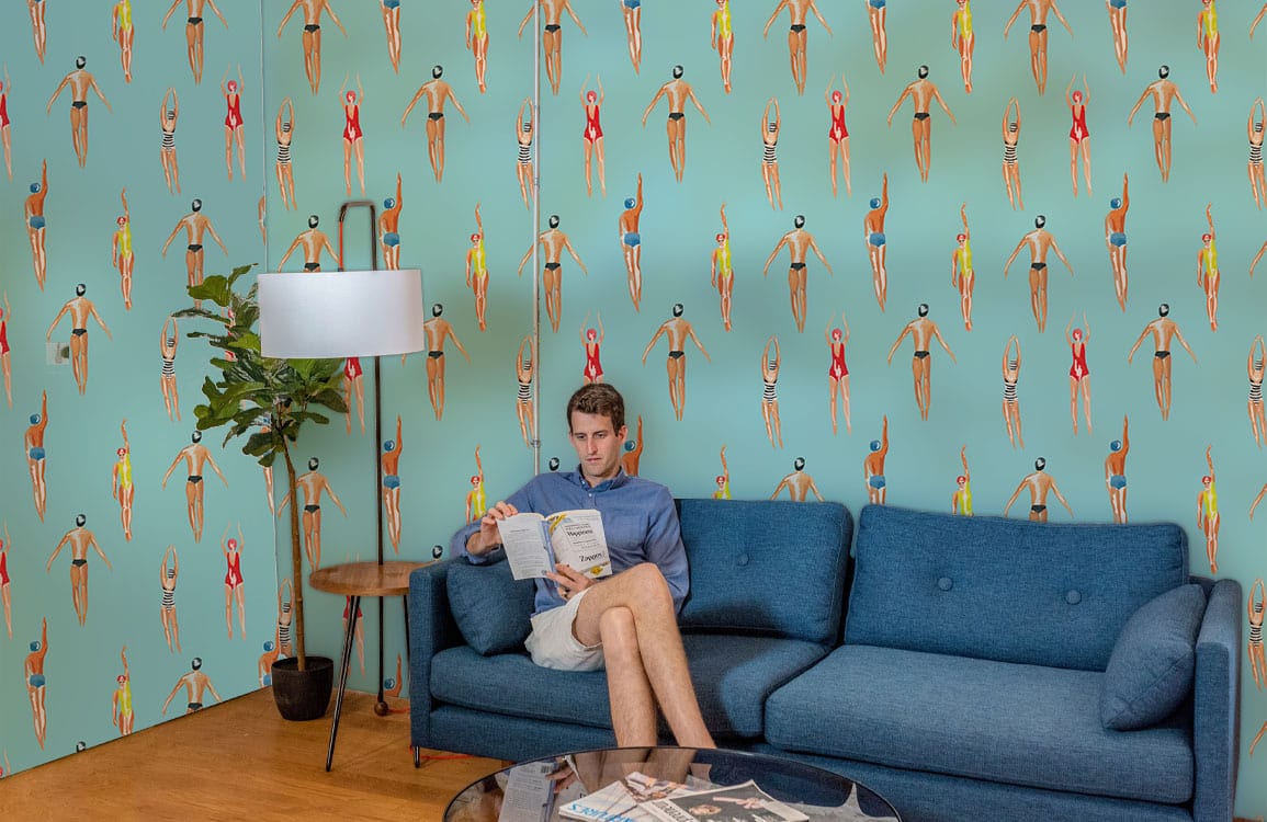 Un homme relaxant sur un canapé bleu avec un papier peint panoramique nageurs dans l’eau
