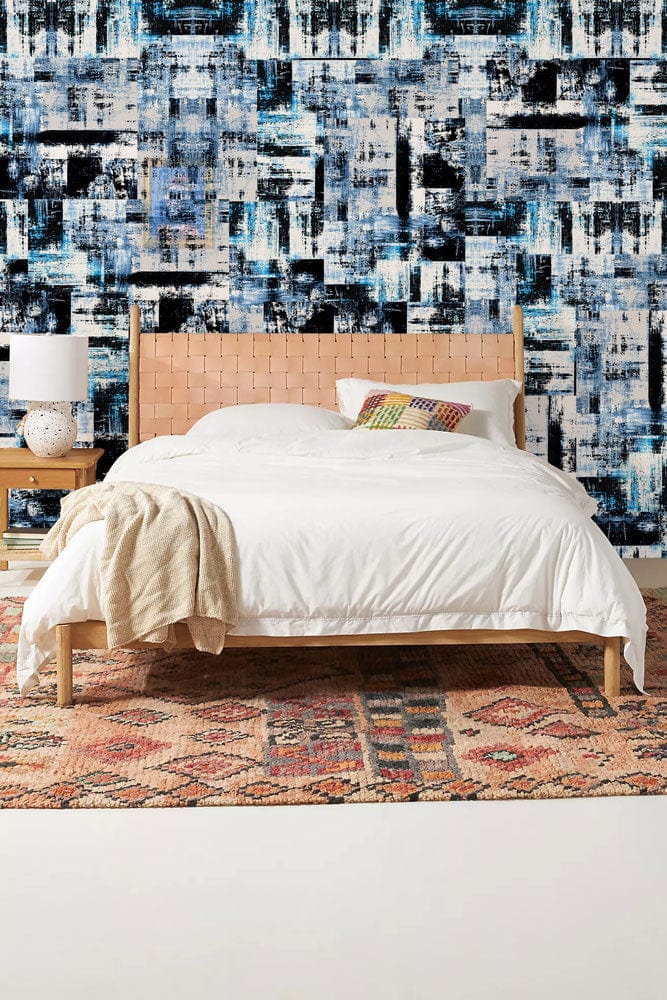 Image d’un lit avec cadre en bois clair et tête de lit en cuir tressé, dans un décor avec papier peint mural à carreaux noirs et bleus