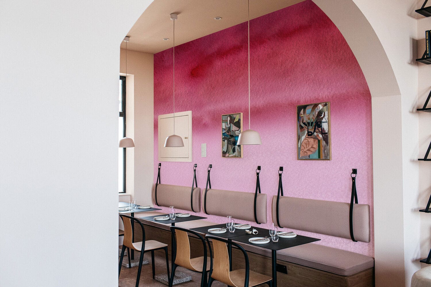 Décor restaurant avec mur mural aquarelle abstraite rose, banquettes claires et tables foncées