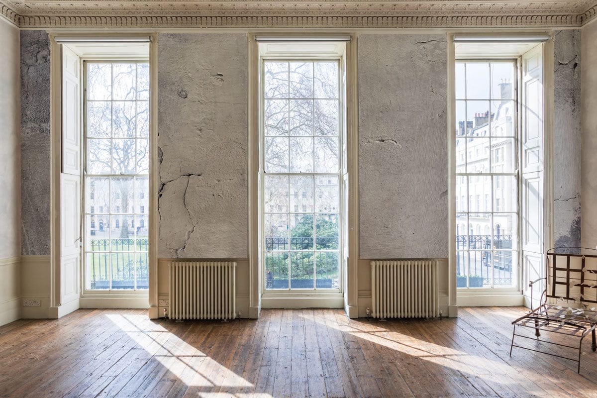 Image d’une pièce vide avec fenêtres, murs usés et papier peint mural blanc moucheté