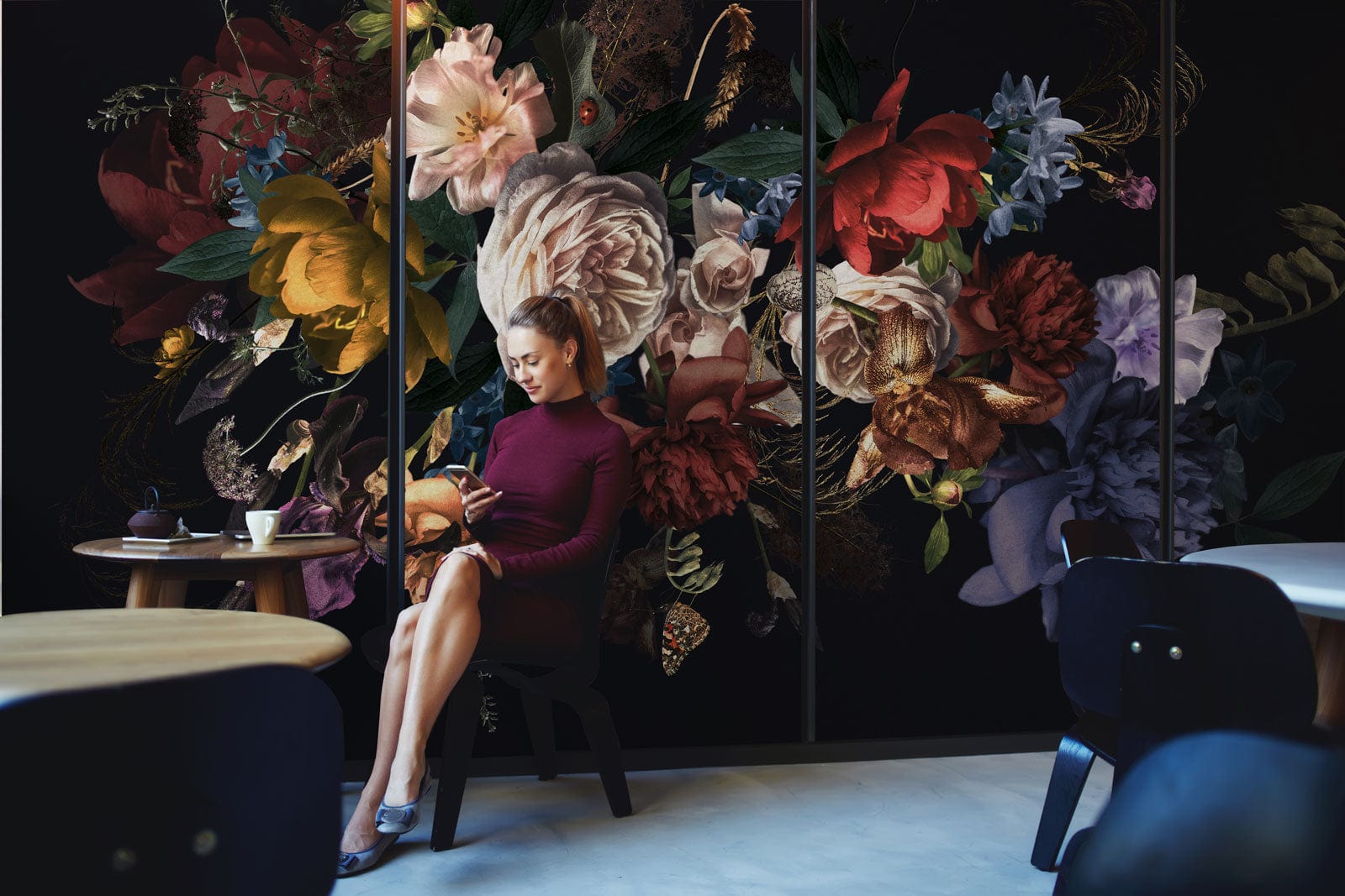 Femme en robe bordeaux assise sur une chaise sombre, décor peint mural roses nocturnes