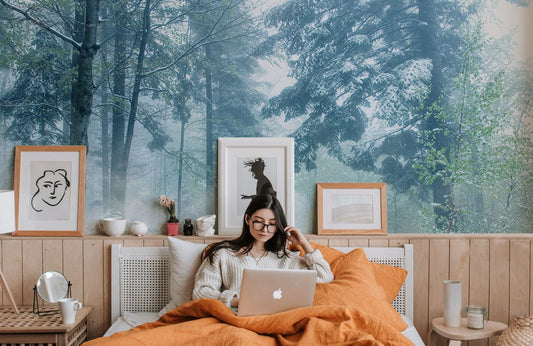 Jeune femme avec longs cheveux noirs et lunettes travaillant sur un ordinateur portable dans un lit, décoration personnalisée avec papier peint mural de montagne enneigée Lane