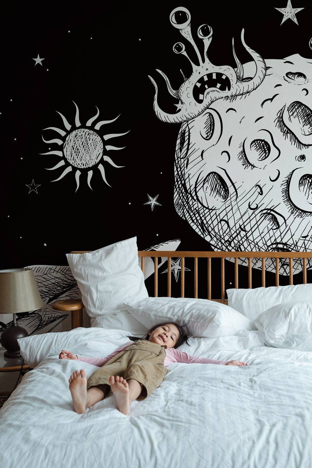 Enfant en salopette sur un lit blanc dans un décor mural espace extra-atmosphérique pour une immersion totale