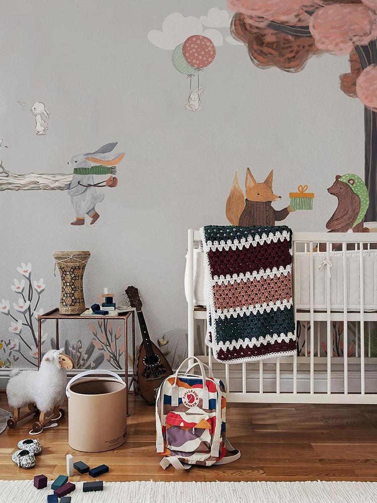 Crib blanc en bois avec couverture crochet, décor mural fête dans la forêt