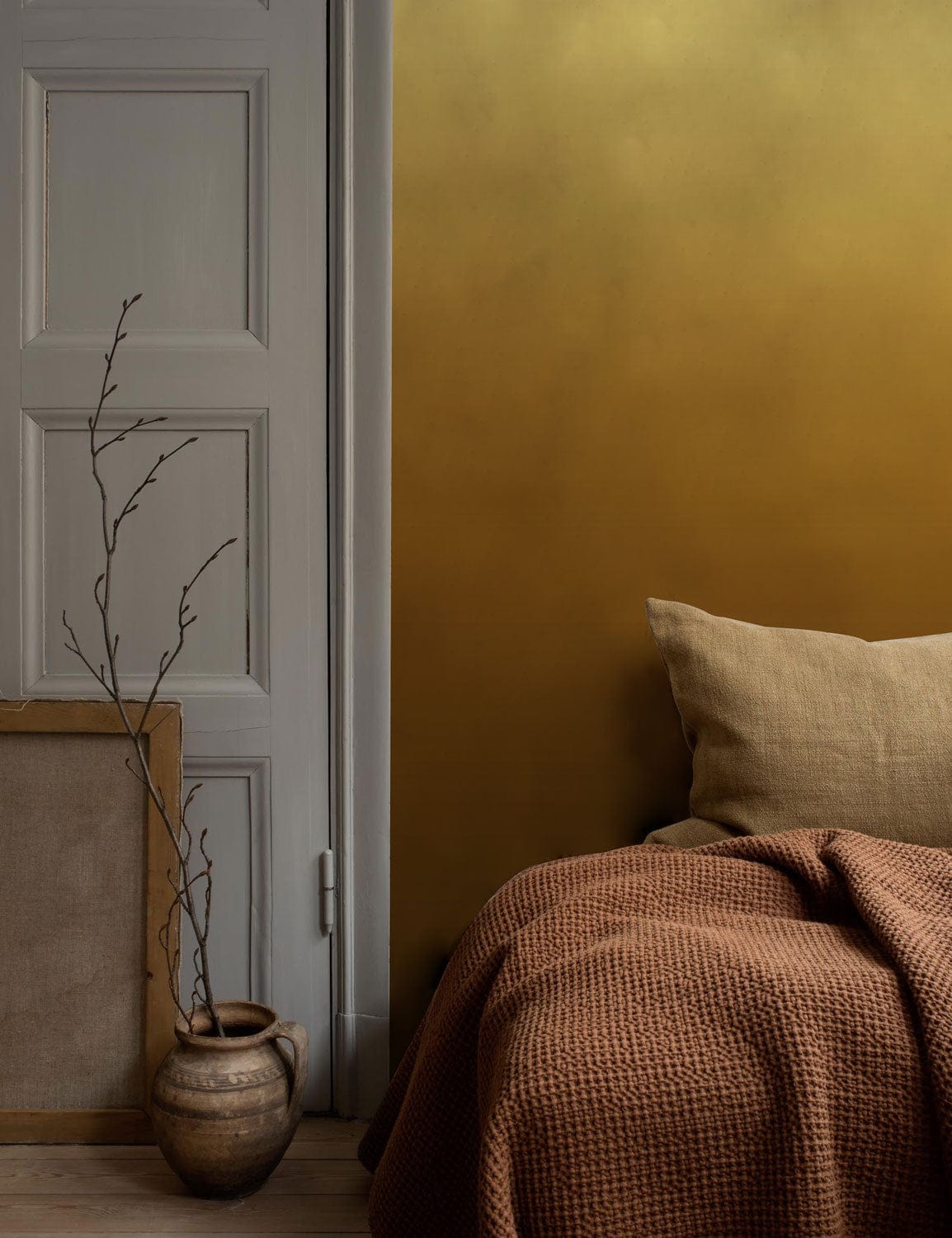 Image d’une chambre avec un lit, oreiller neutre et couverture rustée pour peinture murale ombrée mur ombre brun ambiance chaleureuse