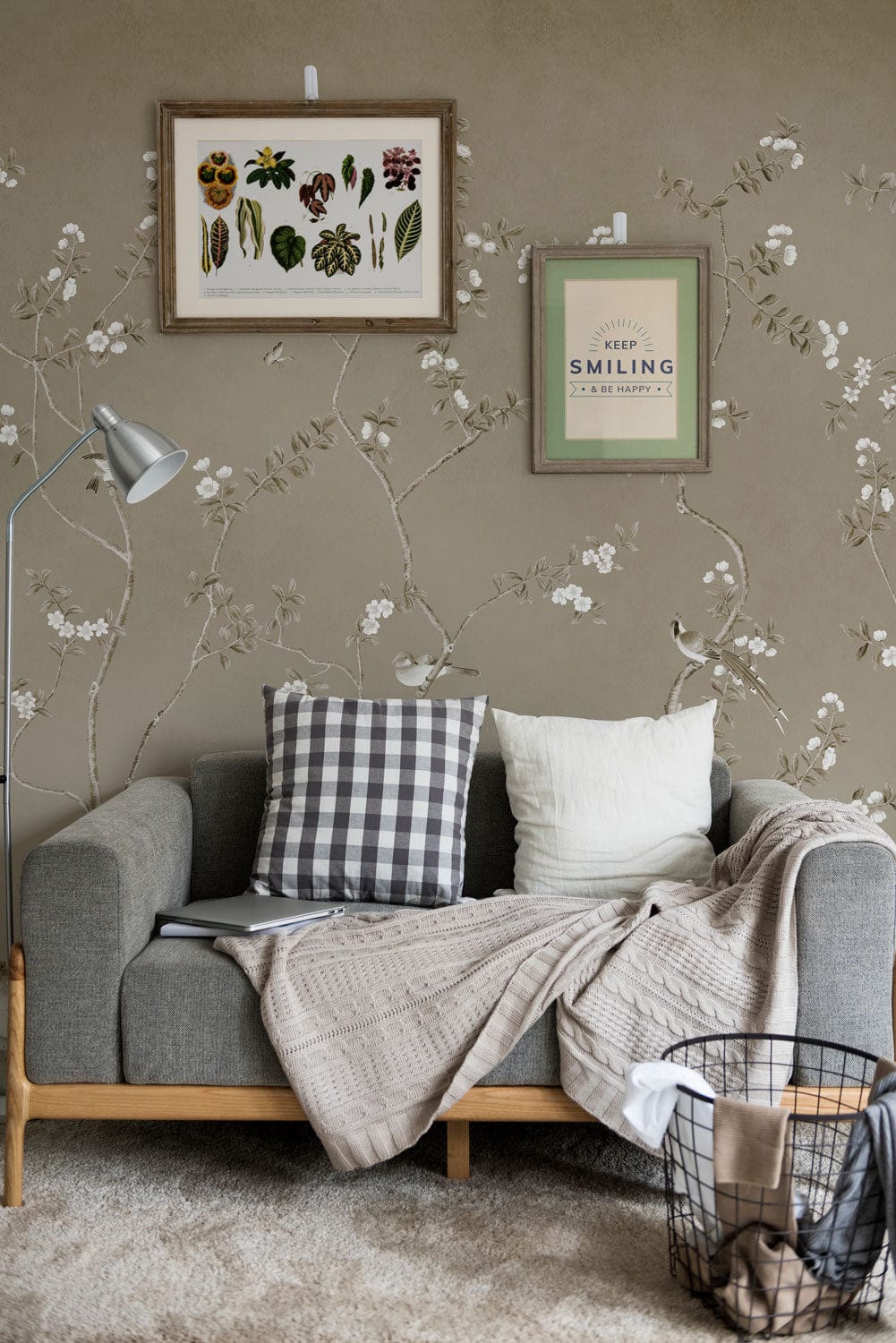 Sofa gris deux places avec coussins et couverture, dans un décor avec papier peint mural Petits Bourgeons