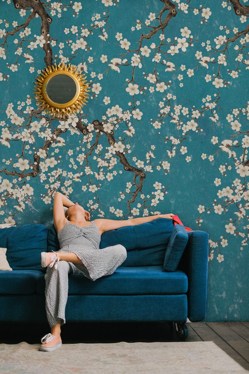 Femme relaxant sur un canapé en velours teal avec papier peint mural Rameau en fleurs