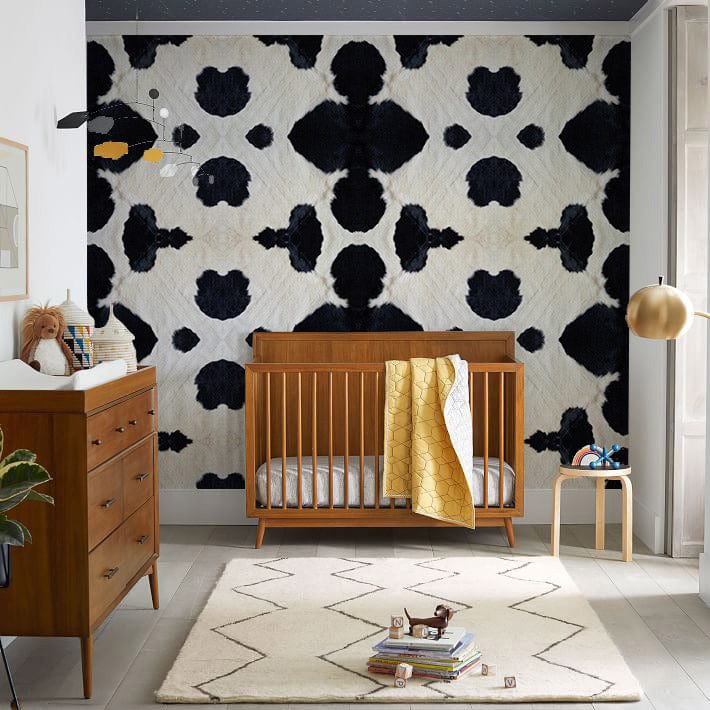 Crib en bois mi-siècle avec papier peint mural texture vache laitière dans une chambre bébé